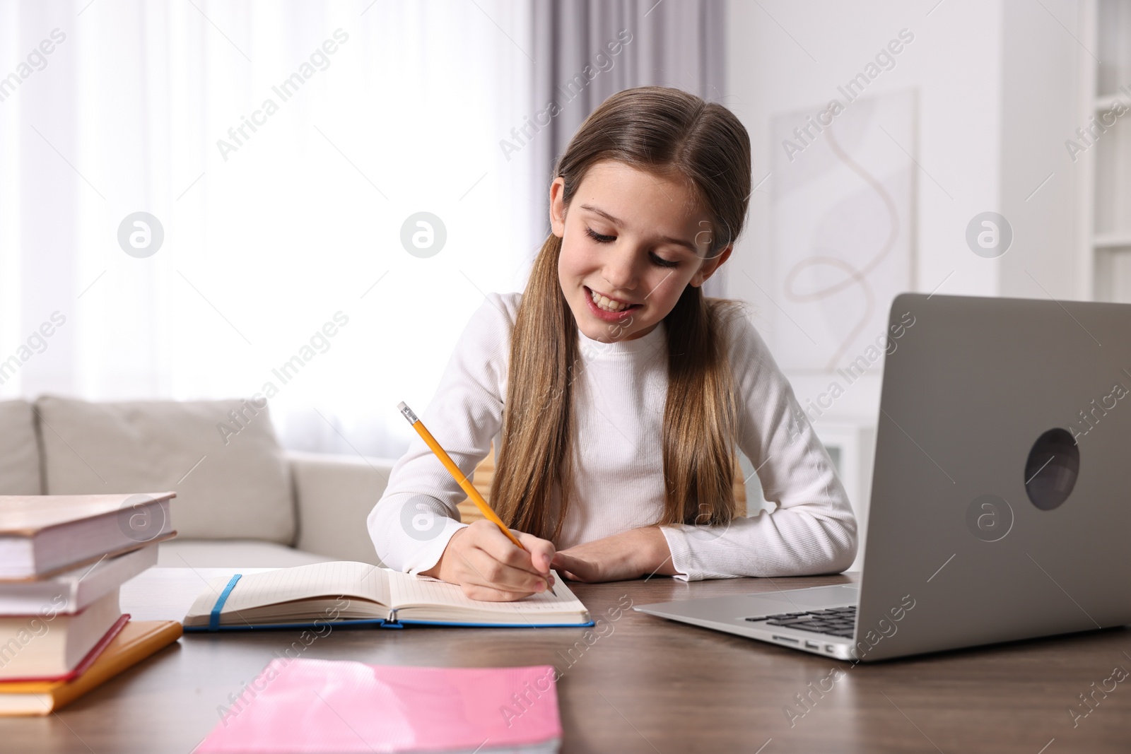 Photo of E-learning. Cute girl taking notes during online lesson at table indoors