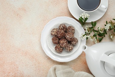 Delicious chocolate candies, cup of hot drink, teapot and blooming branch on beige table, flat lay. Space for text