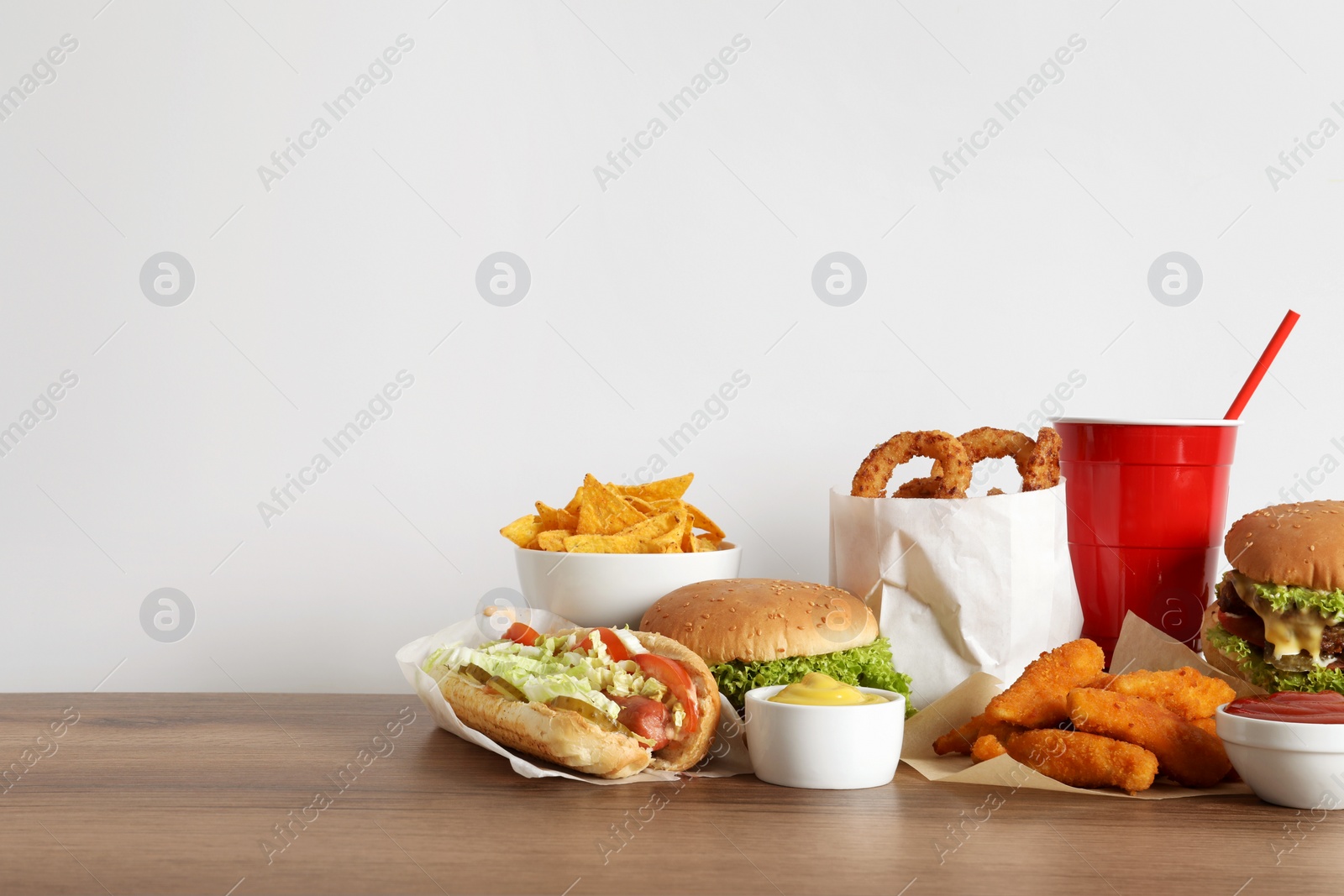 Photo of French fries, burgers and other fast food on wooden table against white background, space for text