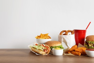 French fries, burgers and other fast food on wooden table against white background, space for text