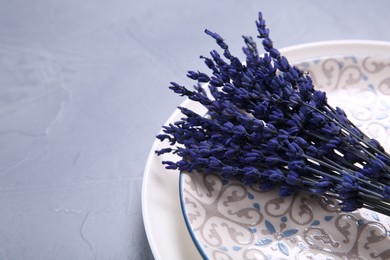 Bouquet of beautiful preserved lavender flowers and plates on light grey textured table, closeup. Space for text