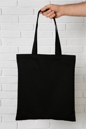 Photo of Man holding cotton shopping eco bag against brick wall. Mockup for design