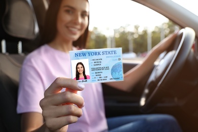 Photo of Happy young woman holding license while sitting in car, focus on hand. Driving school