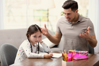 Photo of Father scolding his daughter while helping with homework at table indoors