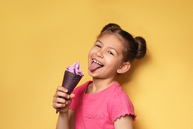 Adorable little girl with delicious ice cream against color background