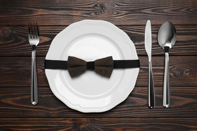 Business lunch concept. Plate with bow tie and cutlery on wooden table, flat lay