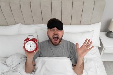Photo of Emotional overslept man with alarm clock in bed, above view. Being late concept