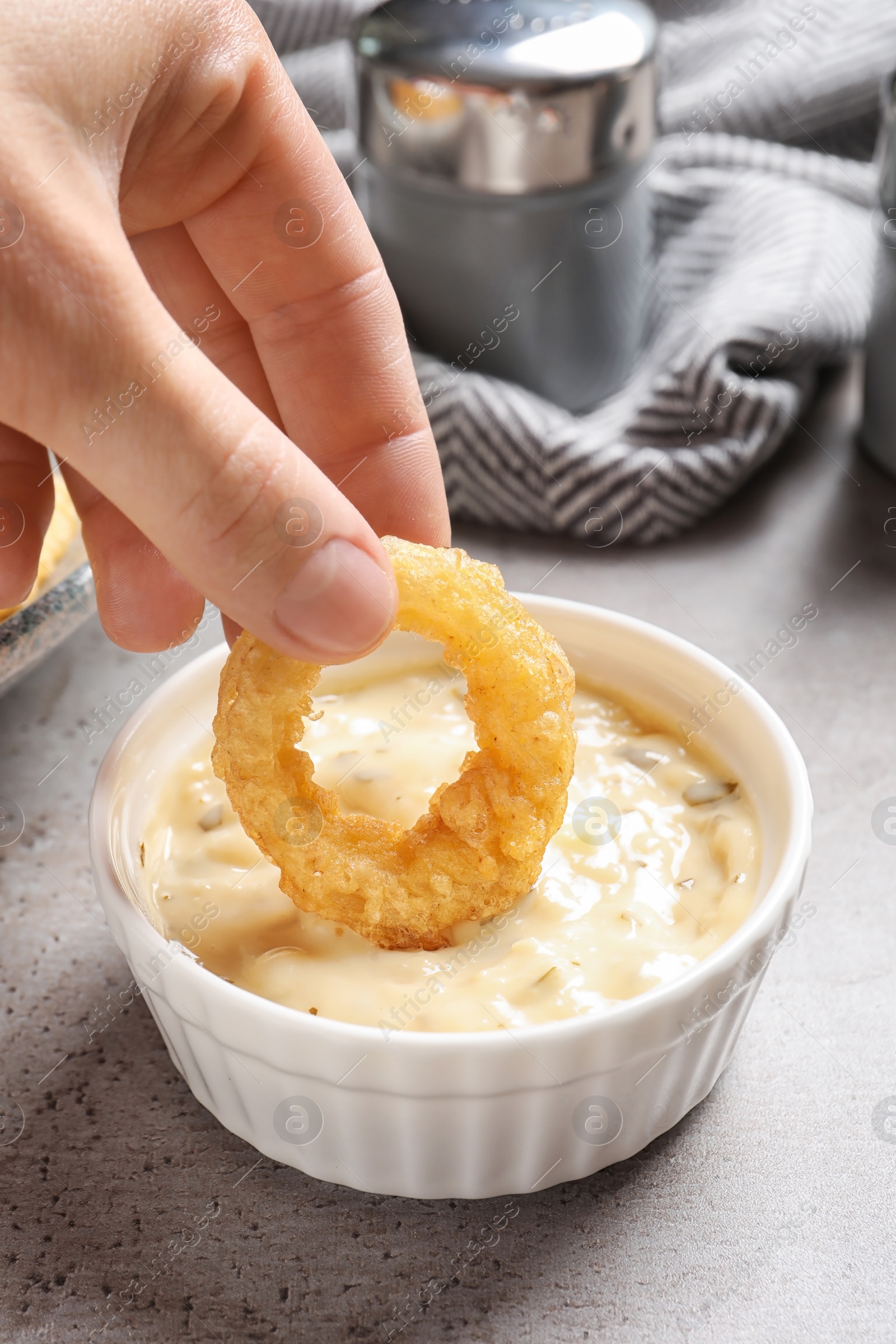 Photo of Woman dipping homemade crunchy fried onion ring in sauce on table, closeup