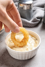 Woman dipping homemade crunchy fried onion ring in sauce on table, closeup