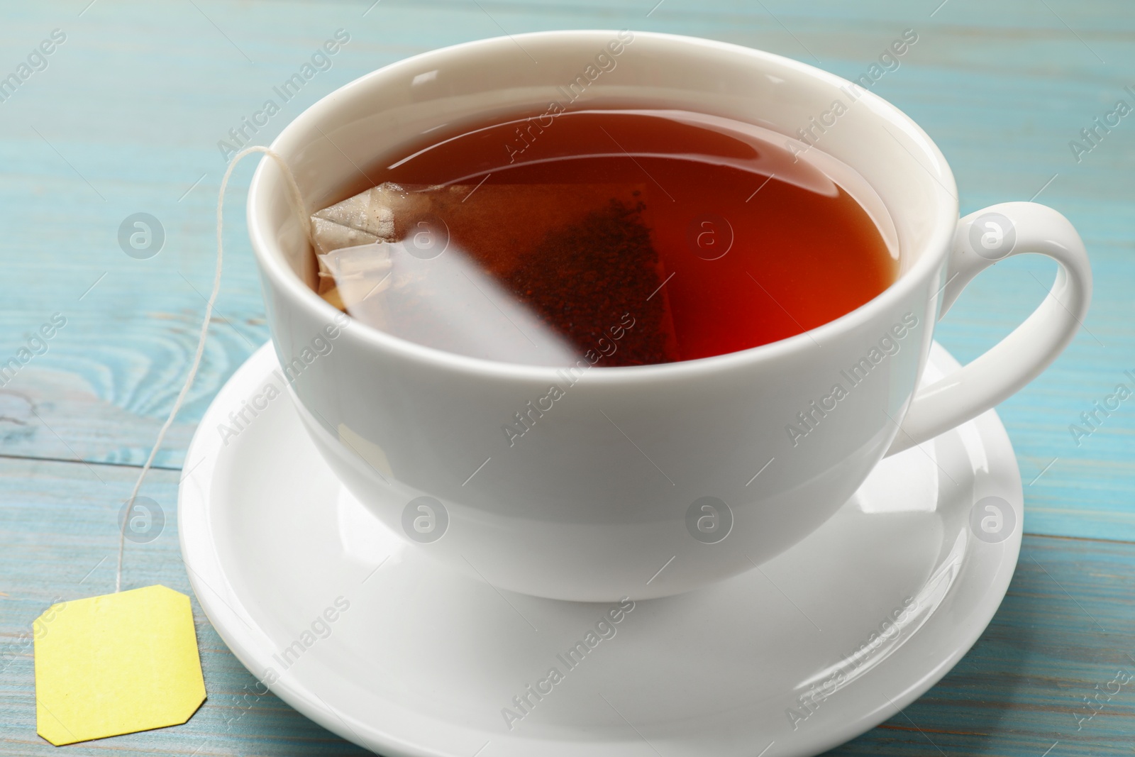 Photo of Tea bag in cup with hot drink on light blue wooden table, closeup