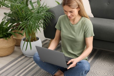 Photo of Woman using laptop on floor in room with beautiful potted houseplants