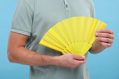 Photo of Man holding hand fan on light blue background, closeup