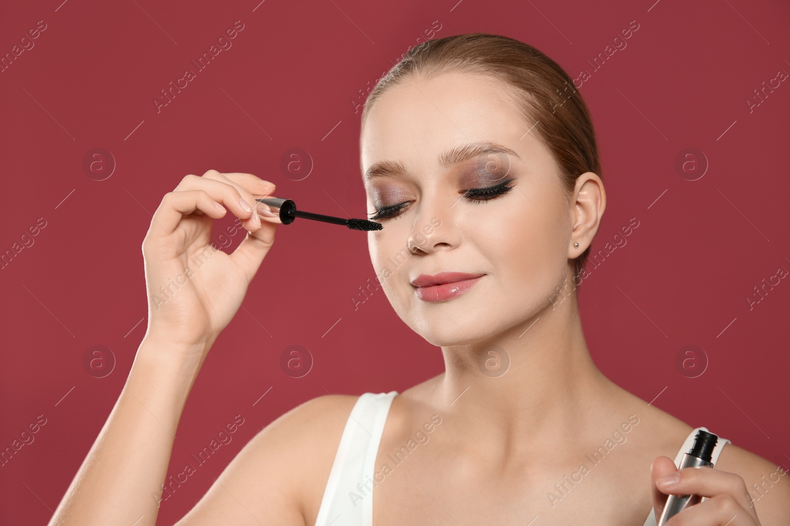 Photo of Beautiful woman applying mascara on pink background. Stylish makeup