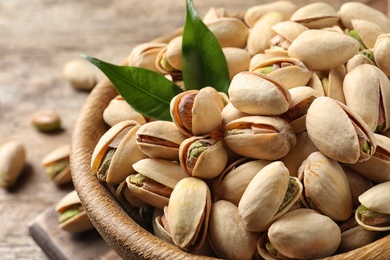 Photo of Organic pistachio nuts in bowl on wooden table, closeup