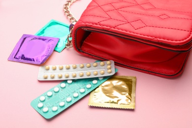 Purse with condoms and birth control pills on pink background. Safe sex