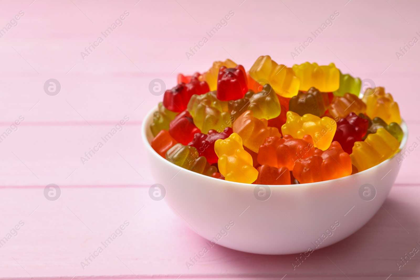 Photo of Bowl with delicious bright jelly bears on pink wooden table, space for text