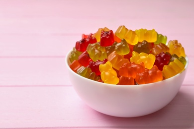 Bowl with delicious bright jelly bears on pink wooden table, space for text