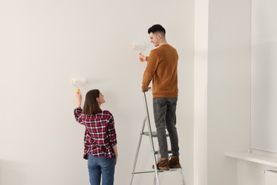 Photo of Young couple painting wall with rollers indoors. Room renovation