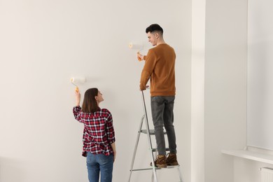 Young couple painting wall with rollers indoors. Room renovation