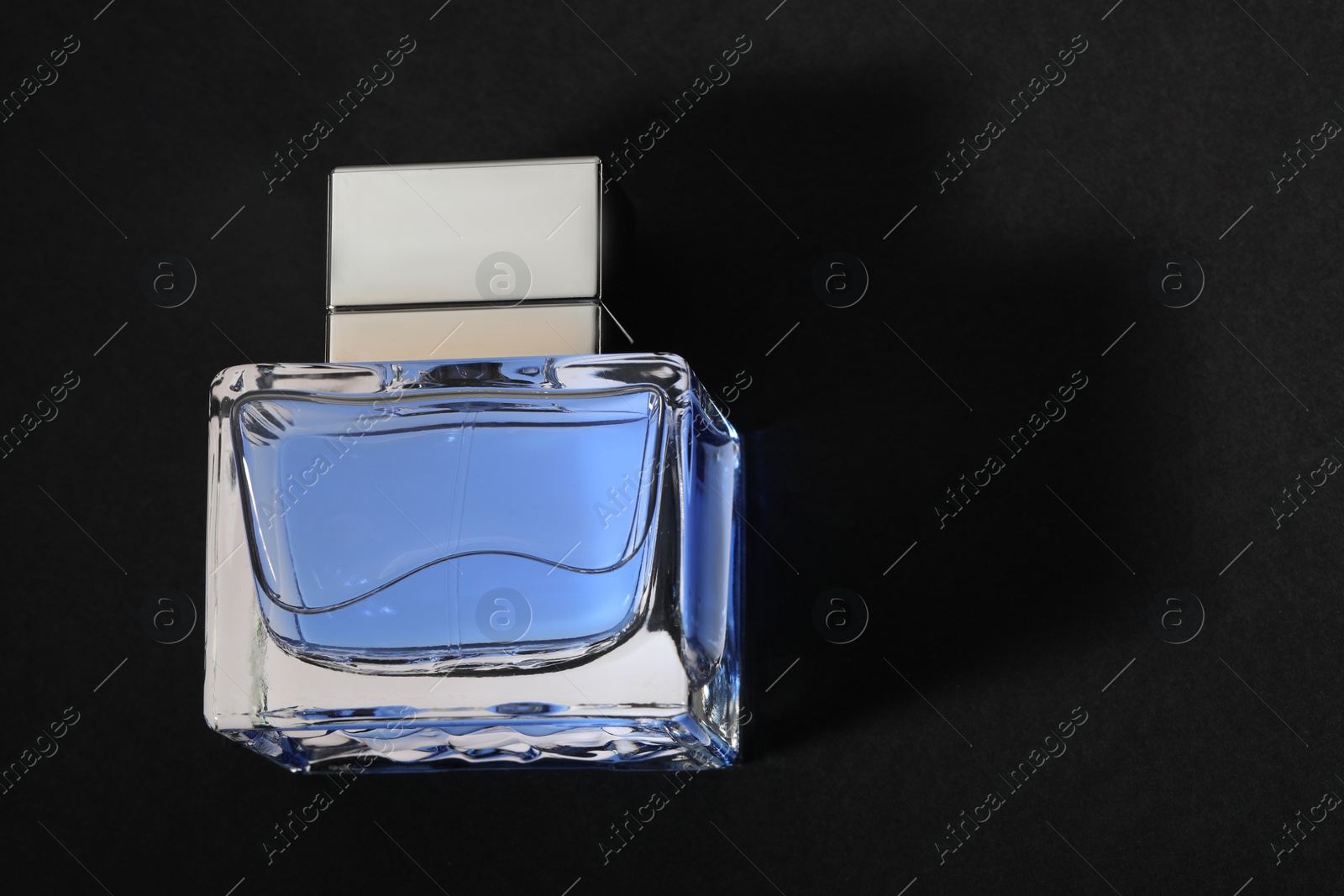 Photo of Blue men's perfume in bottle on black background, top view. Space for text