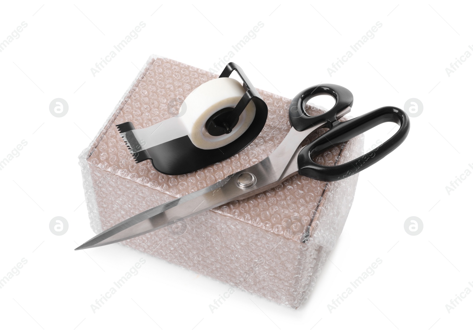 Photo of Cardboard box packed in bubble wrap, scissors and adhesive tape on white background