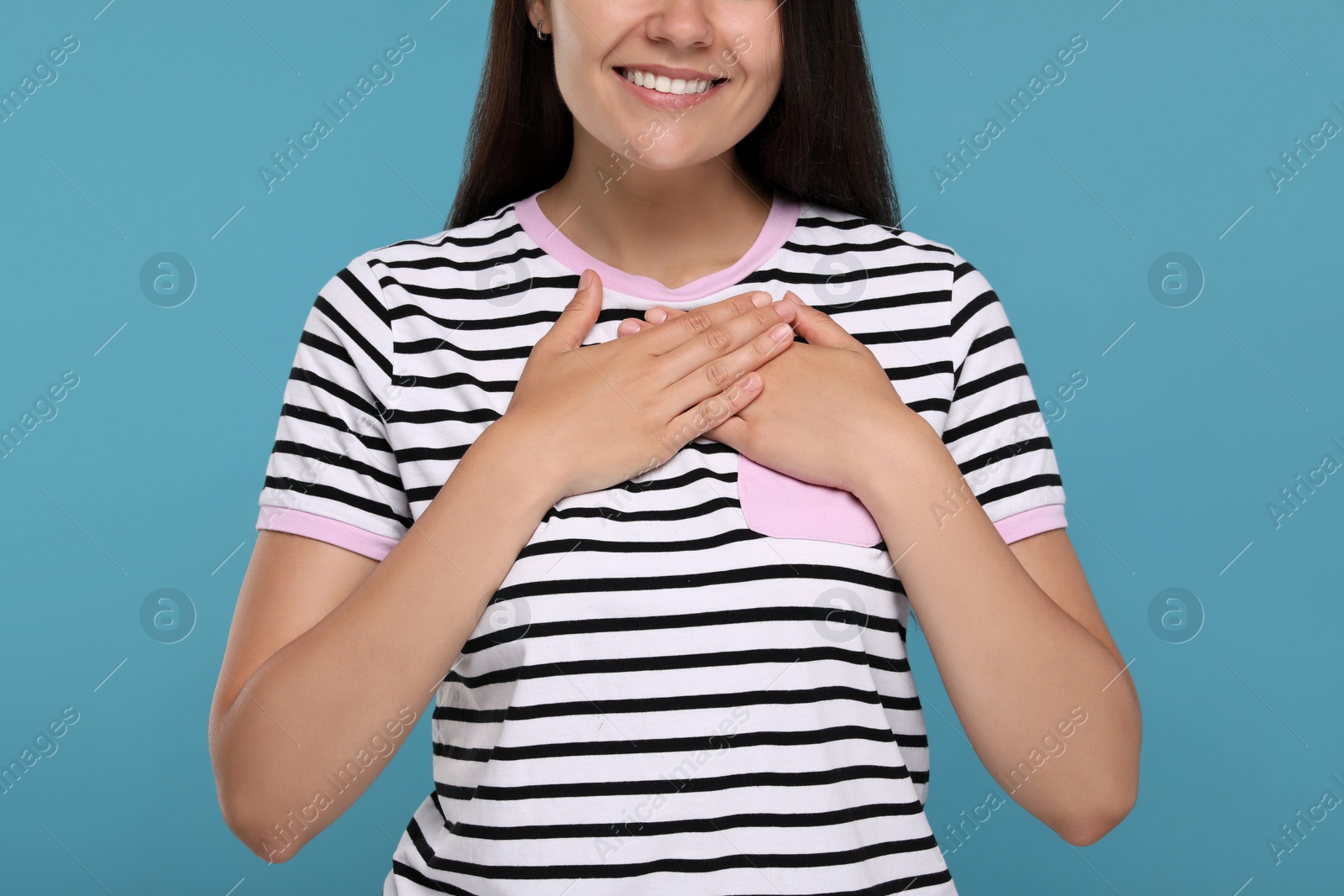 Photo of Thank you gesture. Grateful woman holding hands near heart on light blue background, closeup