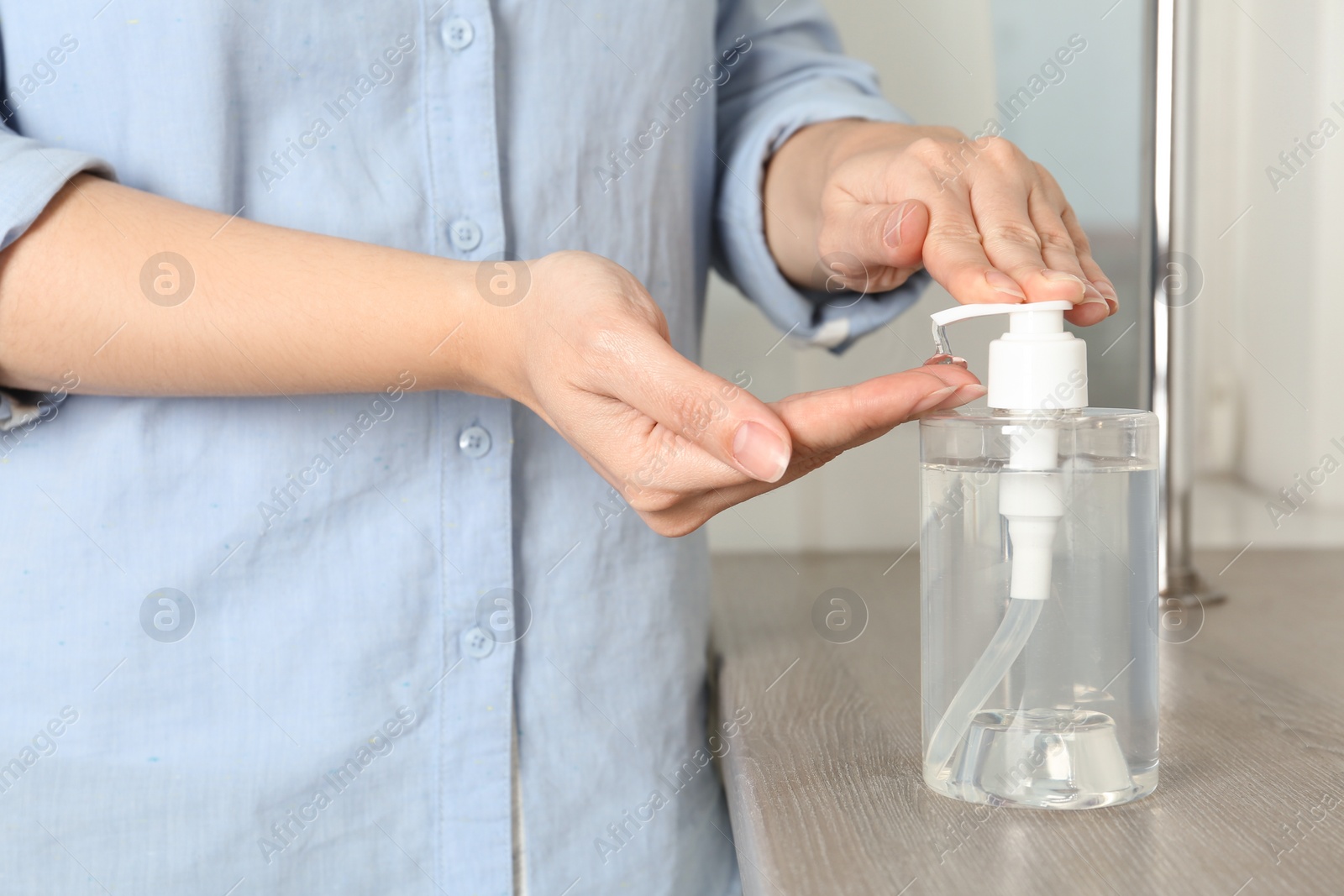 Photo of Woman applying antiseptic gel onto hand at table indoors, closeup. Virus prevention