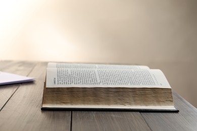 Open Bible on wooden table against beige background. Space for text