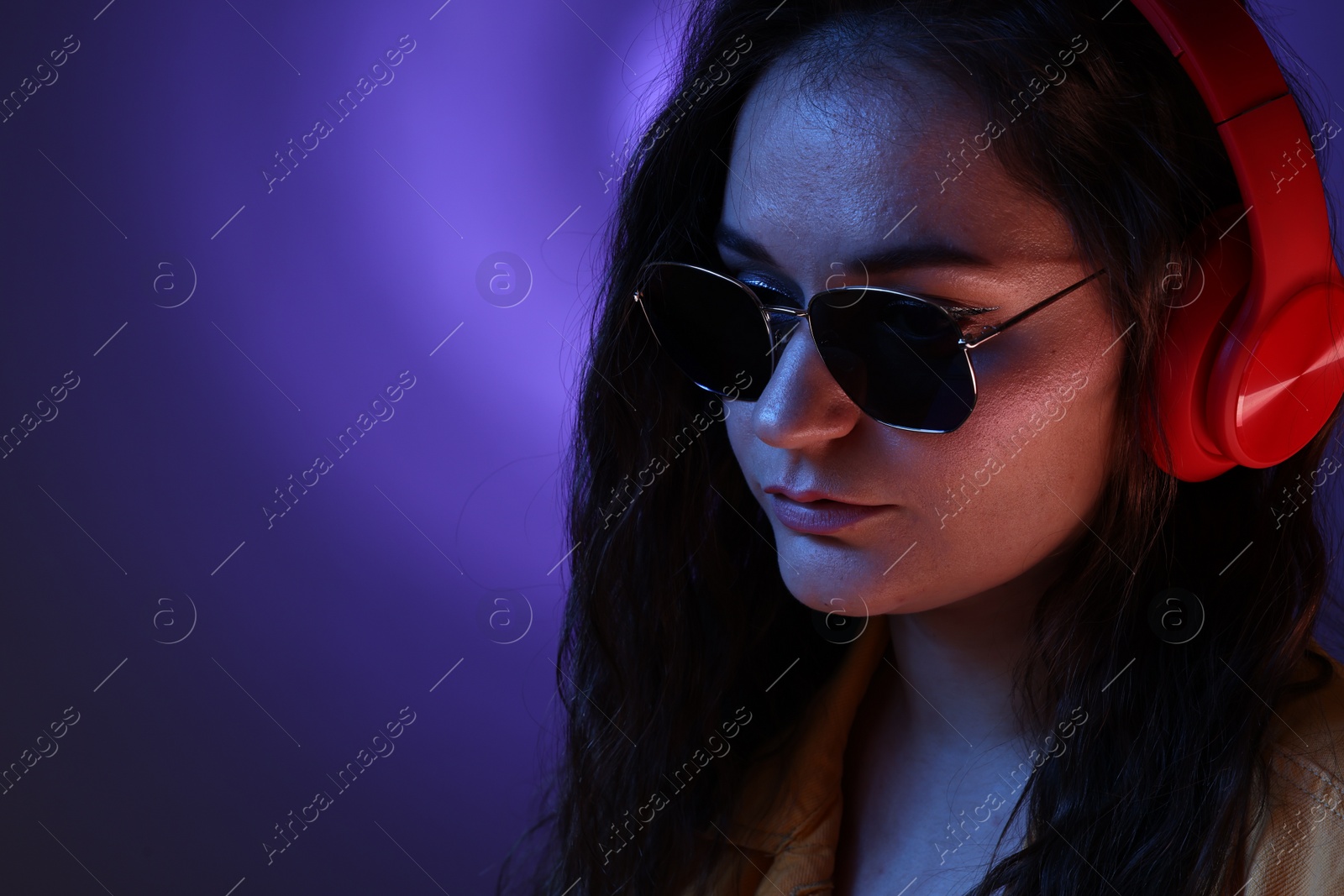 Photo of Portrait of beautiful young woman with headphones on color background with neon lights