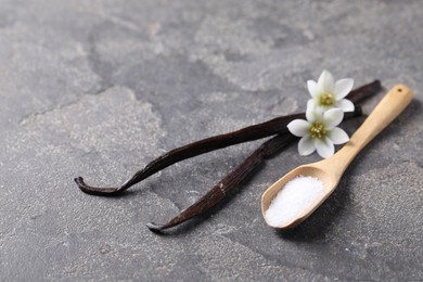 Photo of Spoon with sugar, flowers and vanilla pods on grey textured table, closeup