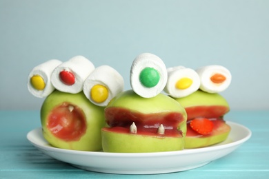 Photo of Delicious apples decorated as monsters on light blue wooden table. Halloween treat