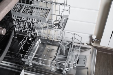 Photo of Open clean empty dishwasher in kitchen, closeup