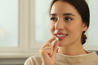 Photo of Young woman taking dietary supplement pill indoors, space for text