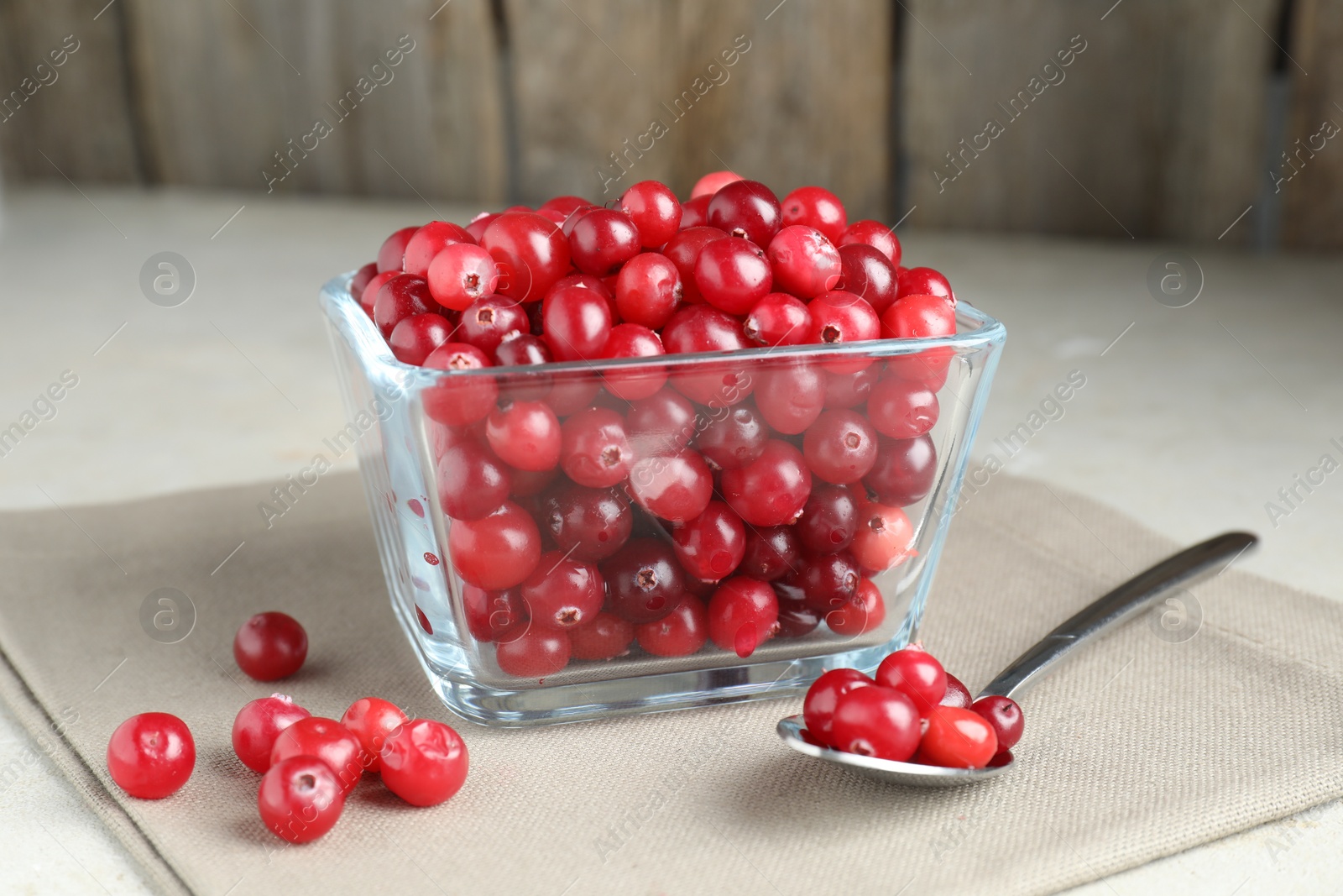 Photo of Cranberries in bowl and spoon on light grey table, closeup