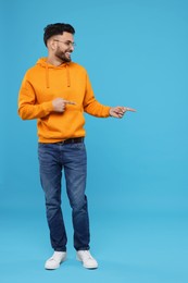 Happy young man pointing at something on light blue background