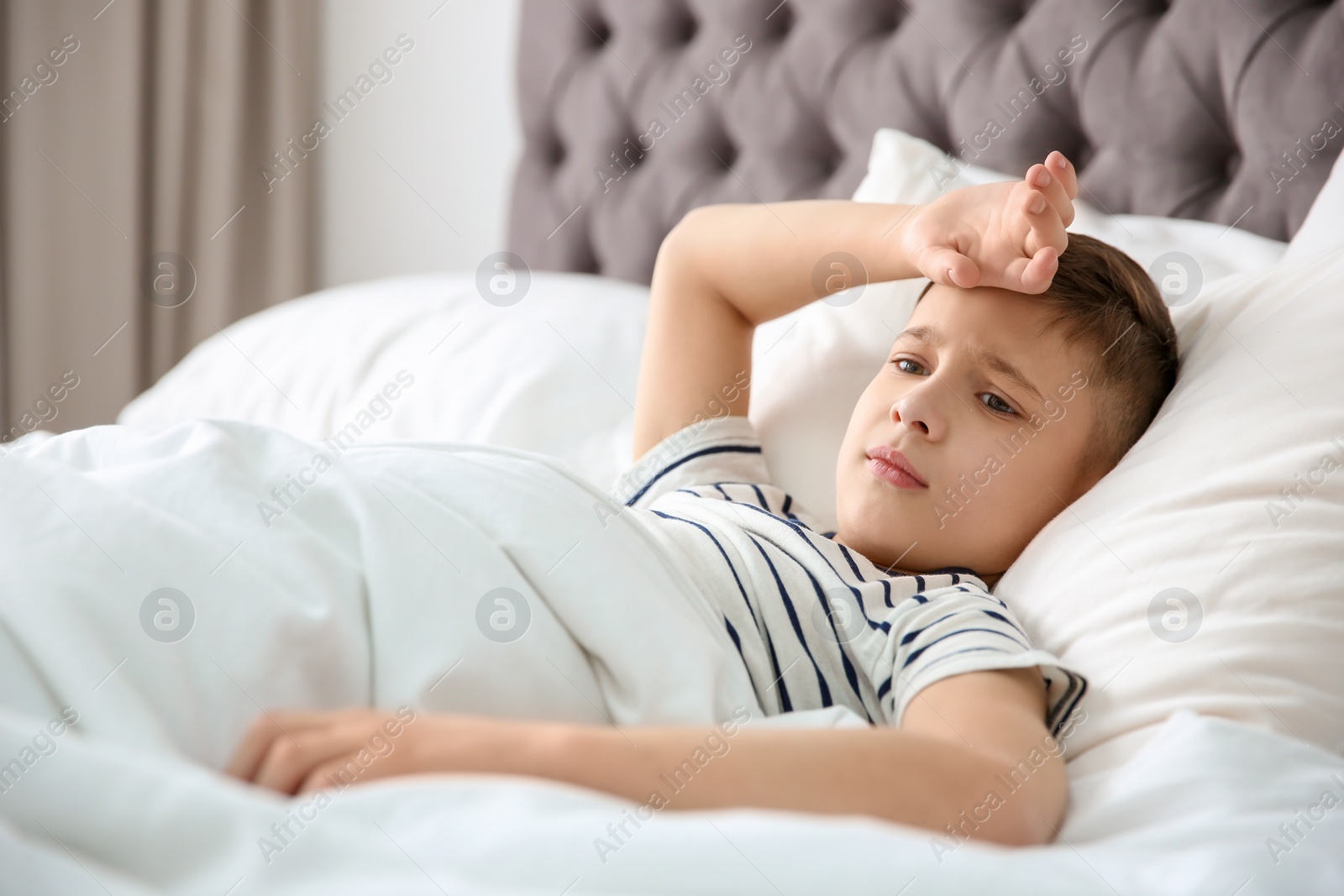 Photo of Little boy suffering from headache while lying in bed at home