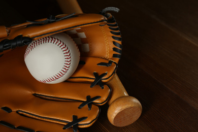 Photo of Leather baseball ball, bat and glove on wooden table, closeup