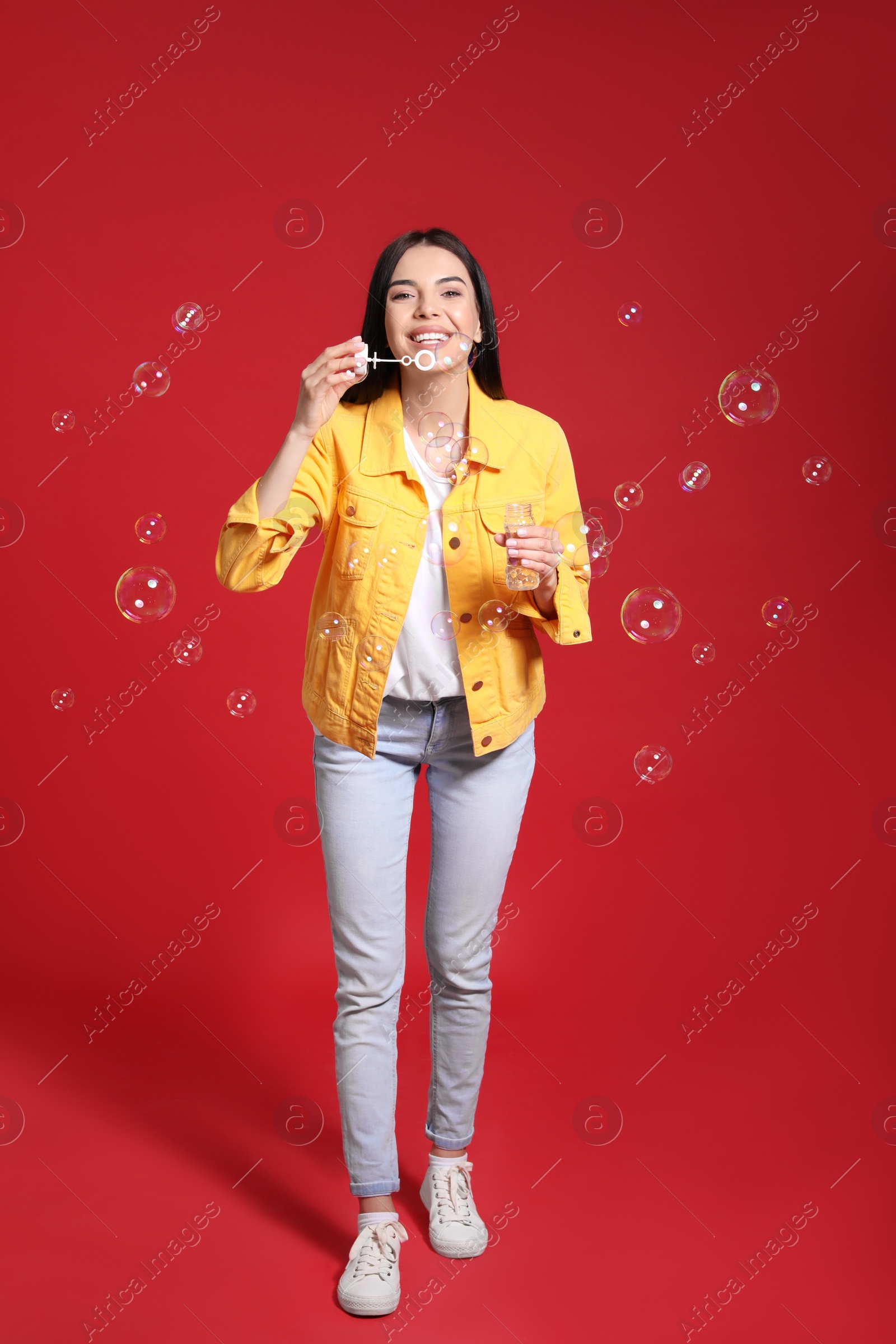 Photo of Young woman blowing soap bubbles on red background