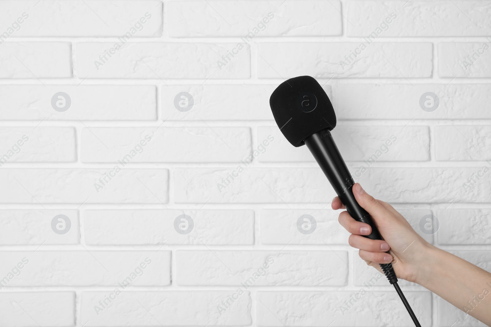 Photo of Woman holding modern microphone near brick wall, closeup. Space for text