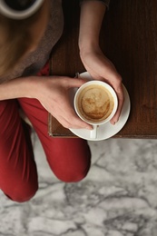 Photo of Young woman with cup of delicious coffee at table