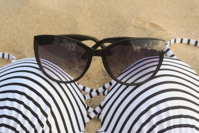 Photo of Beautiful sunglasses and striped swimsuit on sand, closeup