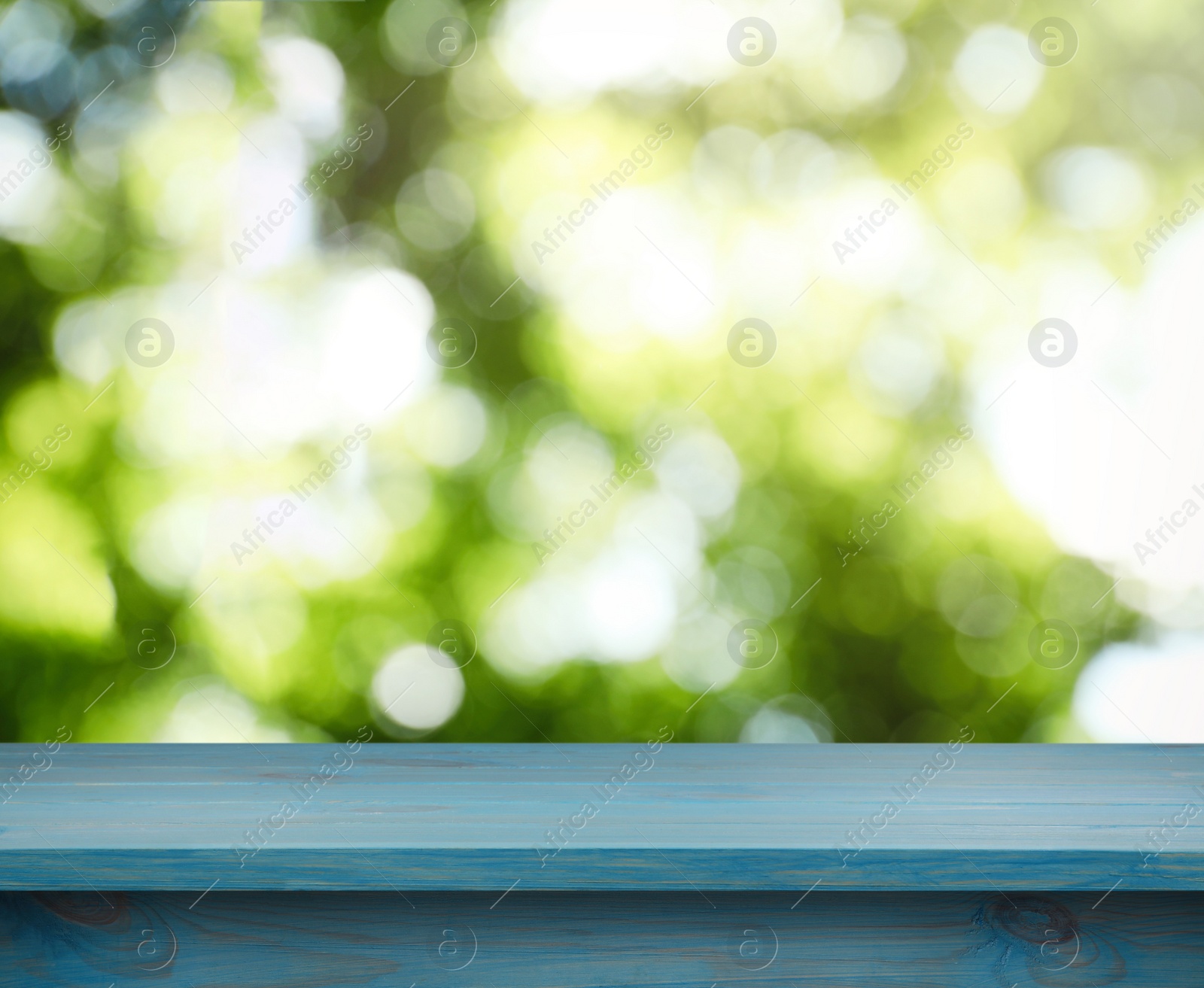 Image of Empty light blue wooden surface against blurred green background. Space for design