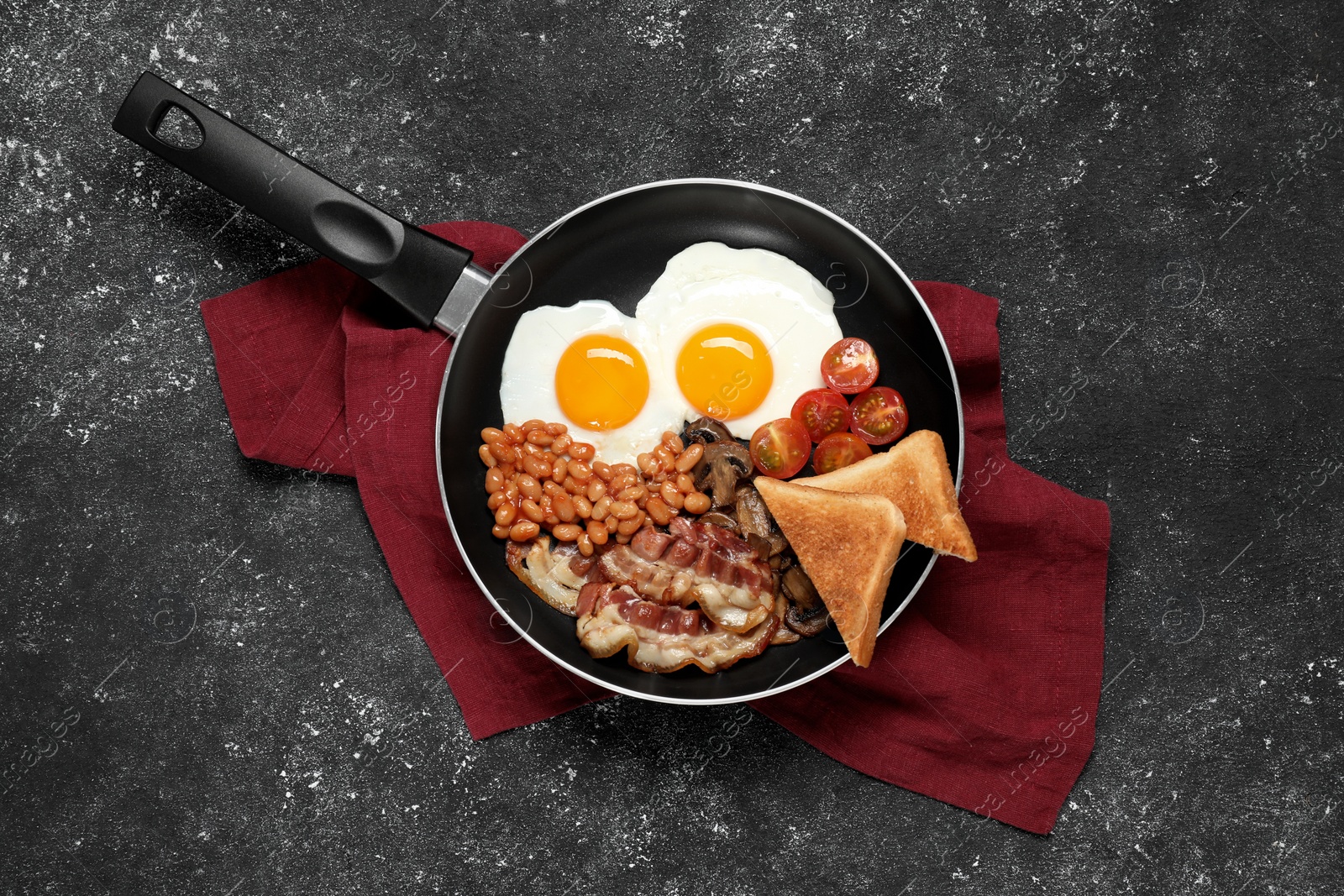 Photo of Frying pan with cooked traditional English breakfast on black textured table, top view