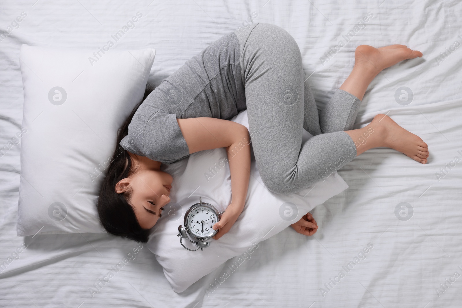 Photo of Young woman with alarm clock suffering from insomnia on bed, top view