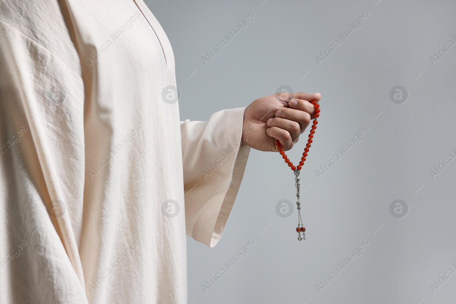 Photo of Muslim man with misbaha on light grey background, closeup