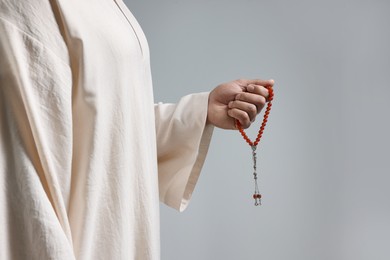 Muslim man with misbaha on light grey background, closeup