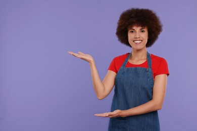 Portrait of happy young woman in apron on purple background. Space for text