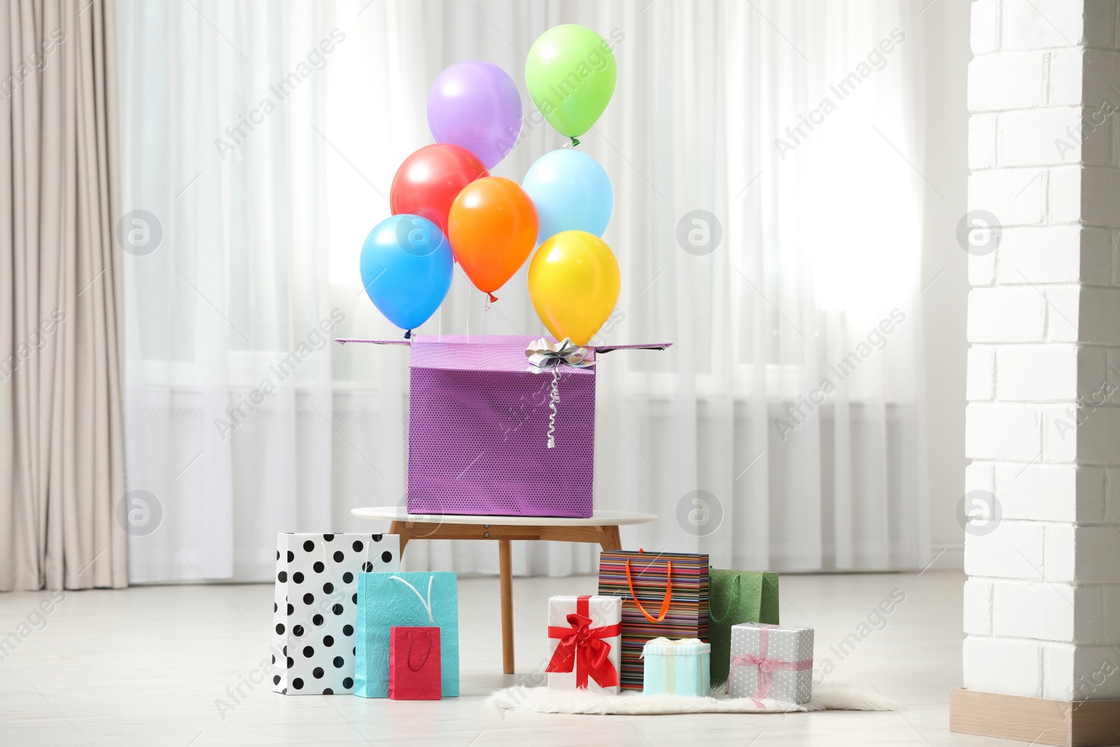 Photo of Gift box with bright air balloons and gift bags indoors