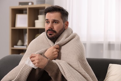 Photo of Sick man with tissue wrapped in blanket on sofa at home. Cold symptoms