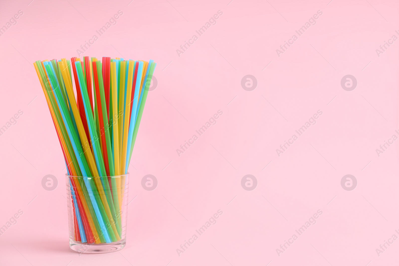 Photo of Colorful plastic drinking straws in glass on pink background, space for text